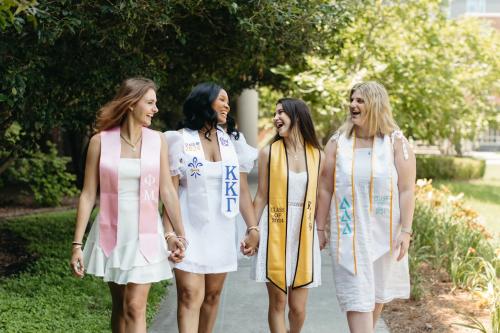 Spring 24 Graduates 4 Women in Graduation Stoles smiling at one another.